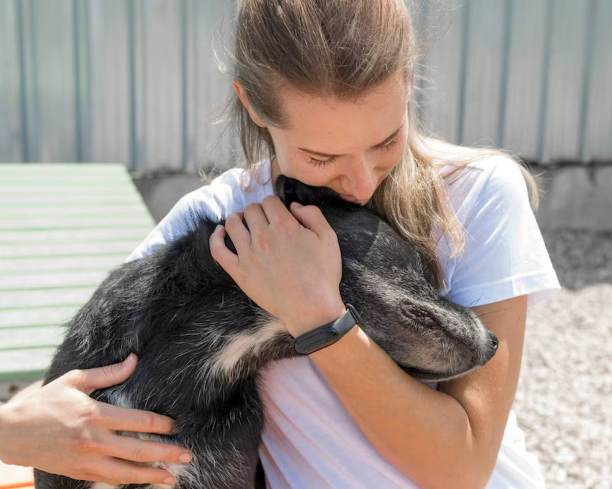 Young woman affectionately hugging a large black dog outdoors.