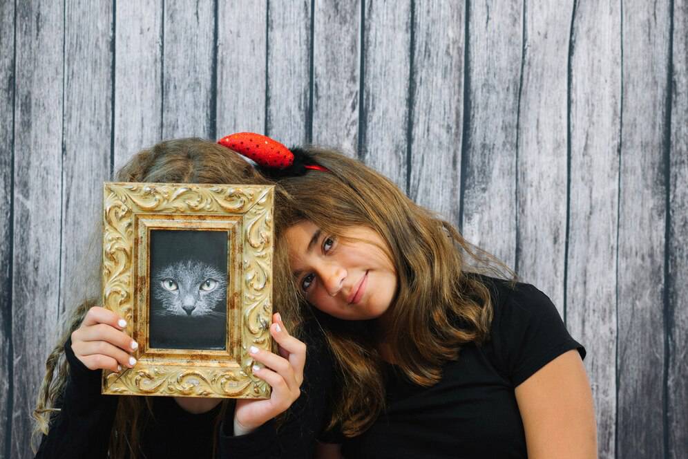 Two girls posing with a framed picture of a cat, against a wooden backdrop.