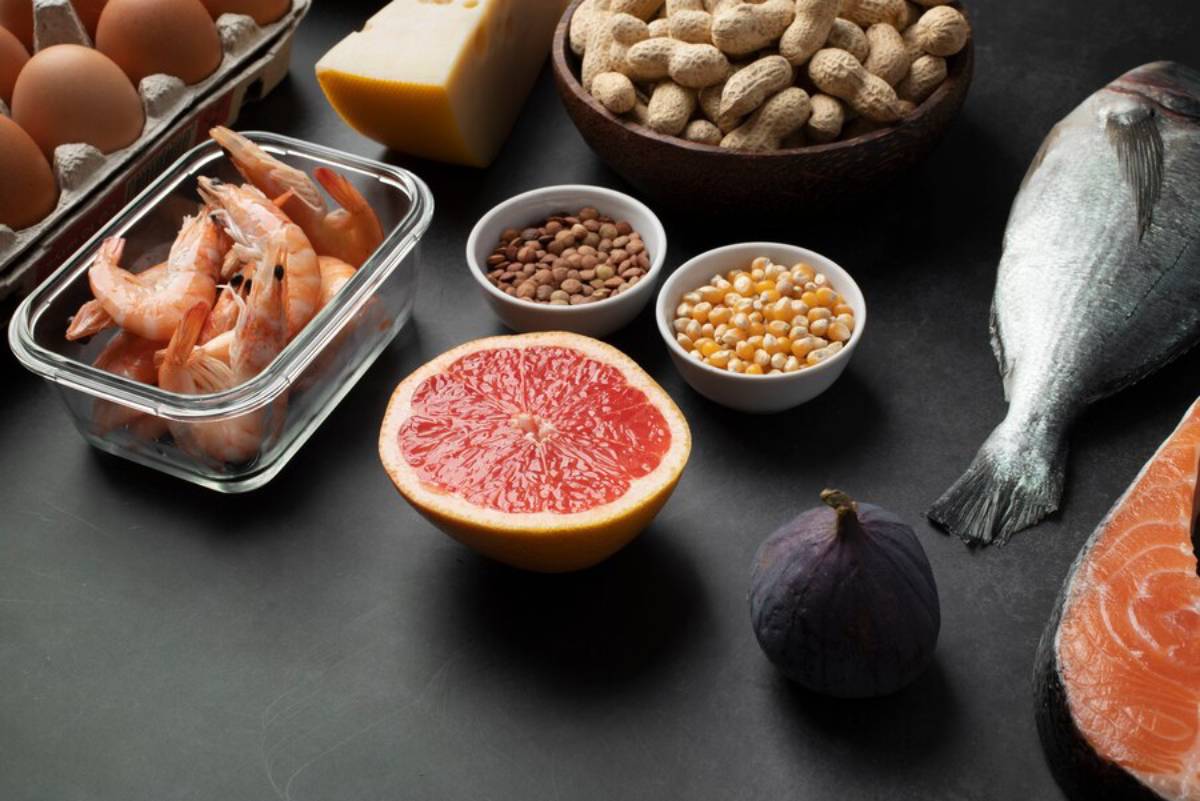 Assorted healthy foods including seafood, eggs, nuts, beans, cheese, and fresh fruits displayed on a dark surface.