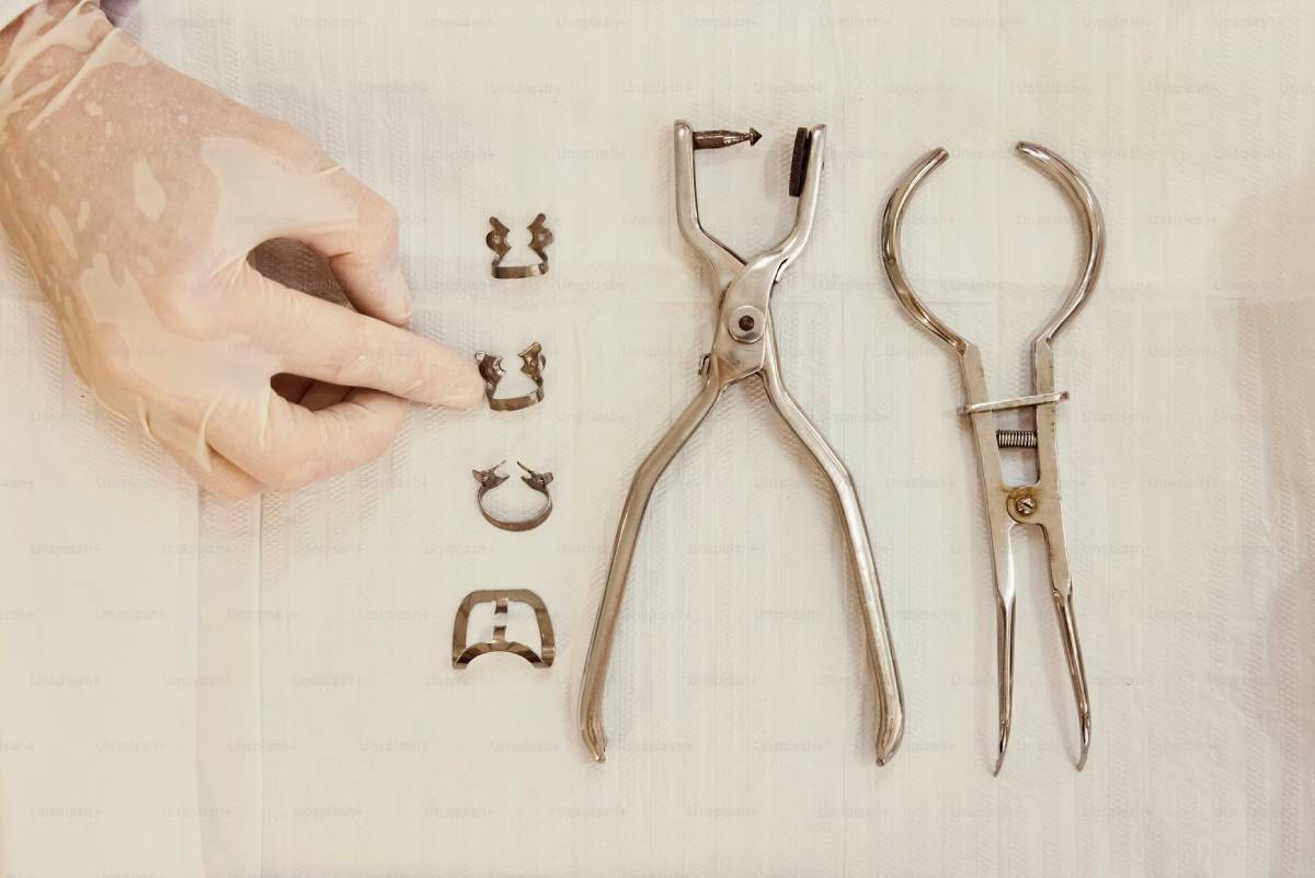 Hand in a glove arranging small metal dental braces pieces next to orthodontic pliers on a textured surface.